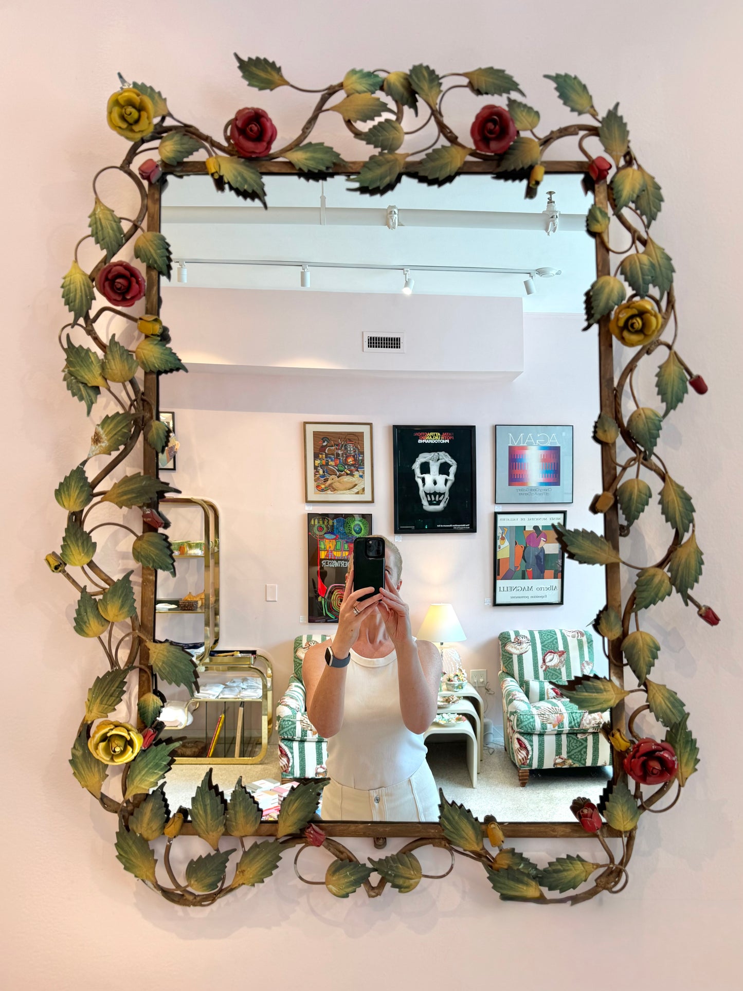 Decorative mirror with floral frame in a room with colorful armchair and framed pictures.
